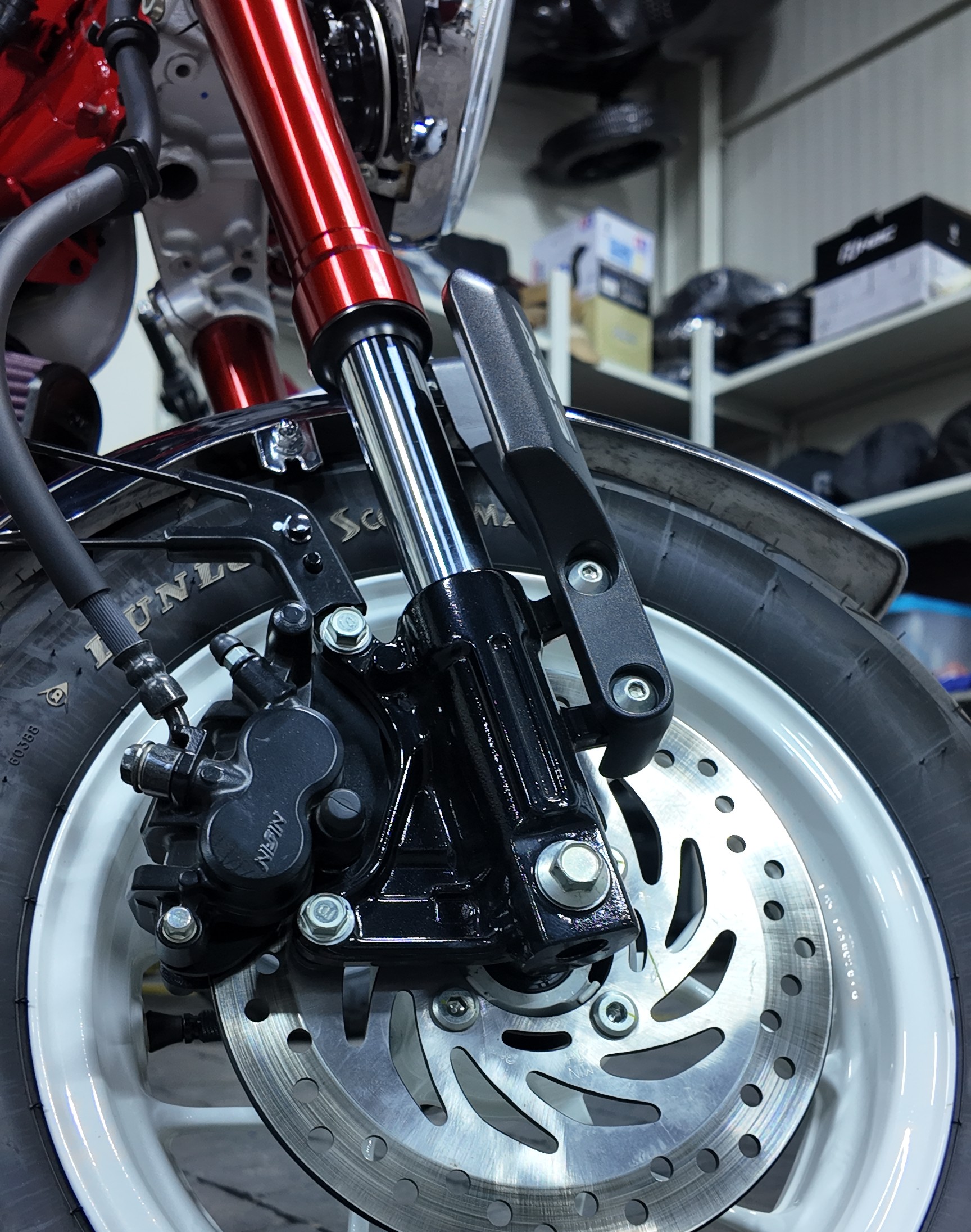 Close-up view of a motorcycle’s front wheel showing detailed brake caliper, disc, and suspension fork components.