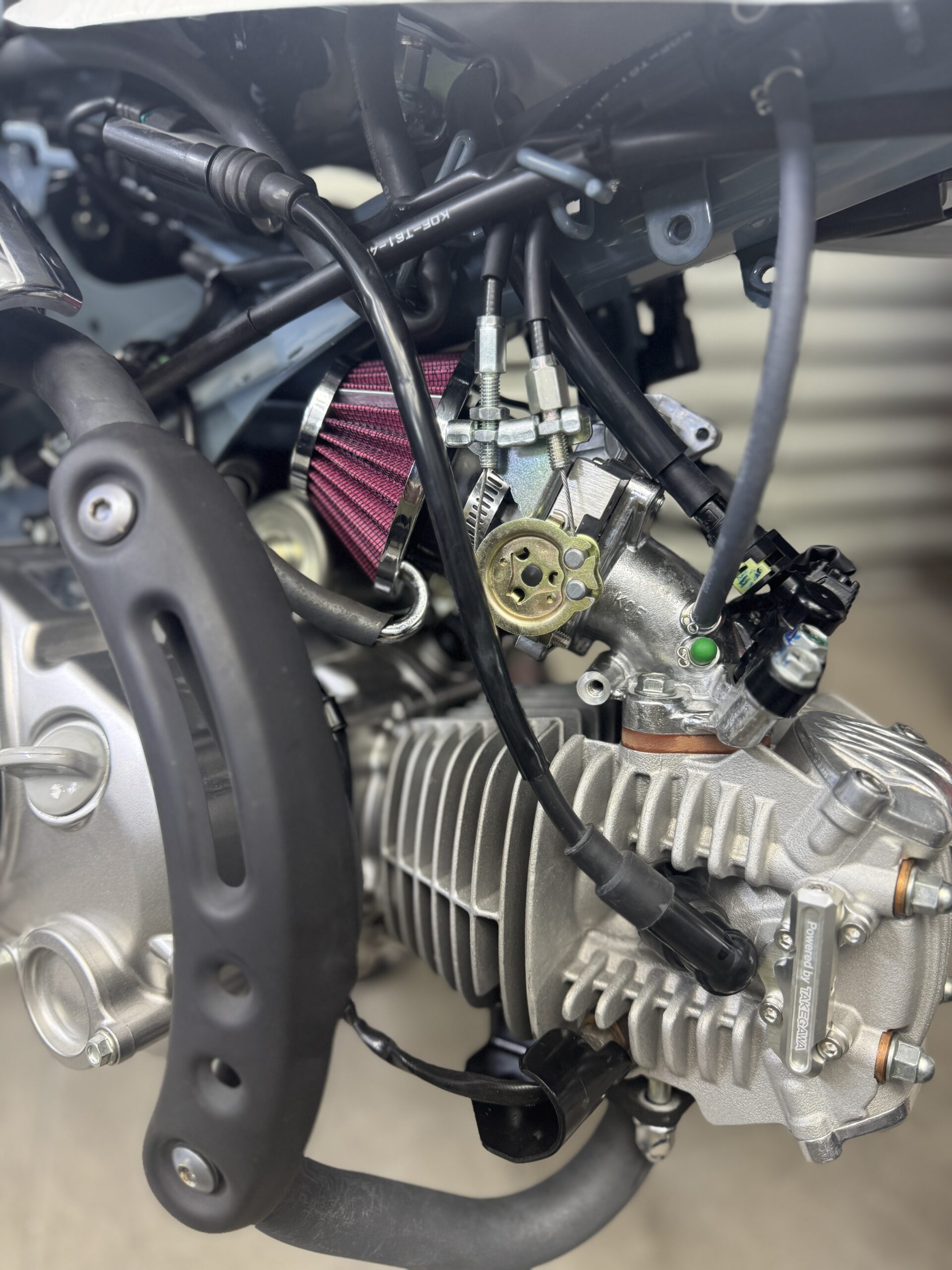 Close-up view of a Motocare Monkey bike’s engine bay, focusing on the electrical wiring, connectors, and lighting fix components intertwined with the carburetor and air filter.